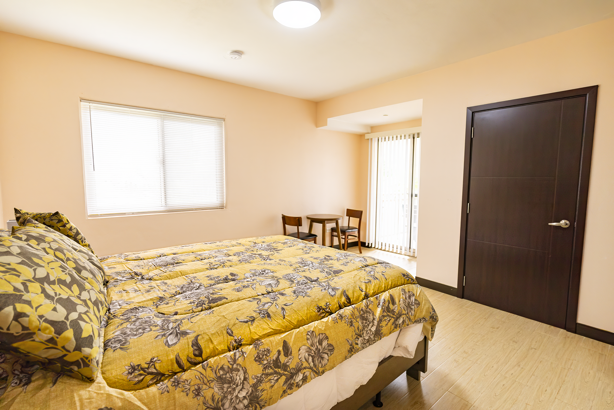 Side view of the bedroom with a bed with yellow comforter that has access to a big window